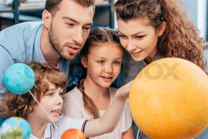 Family exploring solar system model for school project, stock photo