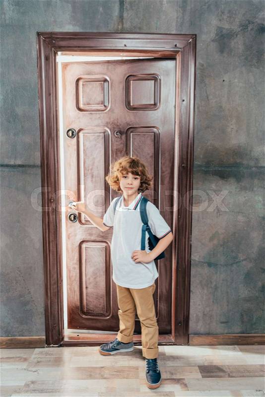 Cute little boy going to school, standing next to door, stock photo