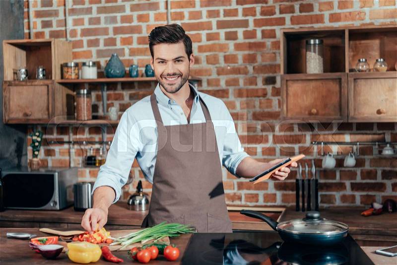 Happy young man cooking with tablet, stock photo