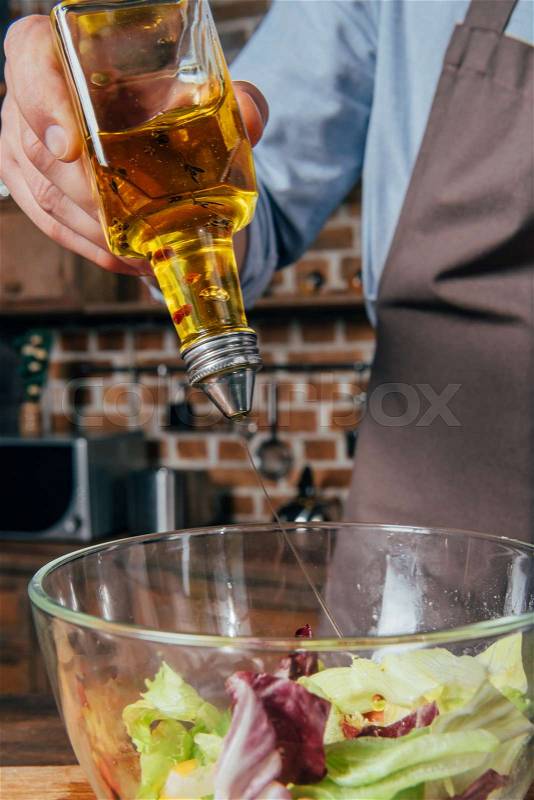 Close-up shot of man adding olive oil into salad, stock photo