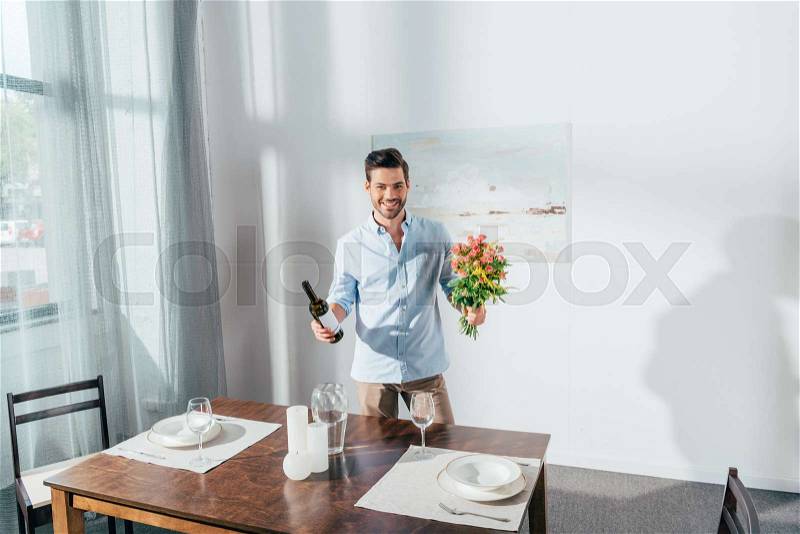 Smiling young man with bouquet of flowers and wine, stock photo