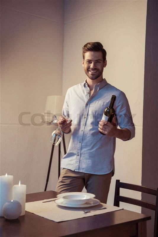 Happy young man with wine bottle and glasses, stock photo