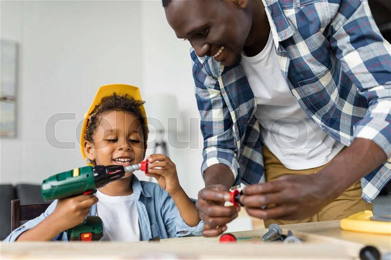 Happy african-american father and son playing with toy tools and laughing, stock photo