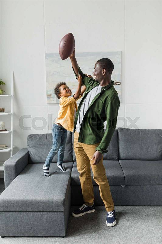 Father and son playing with american football ball at home, stock photo