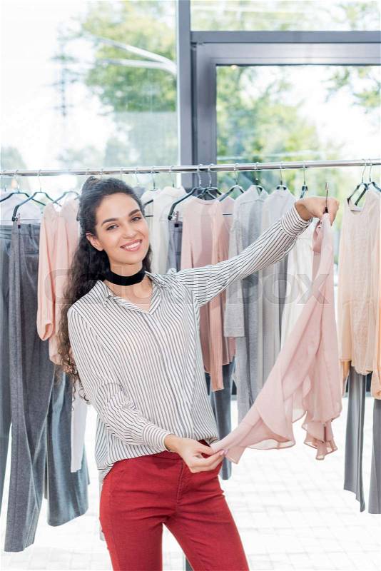 Beautiful smiling woman choosing clothes in showroom, stock photo