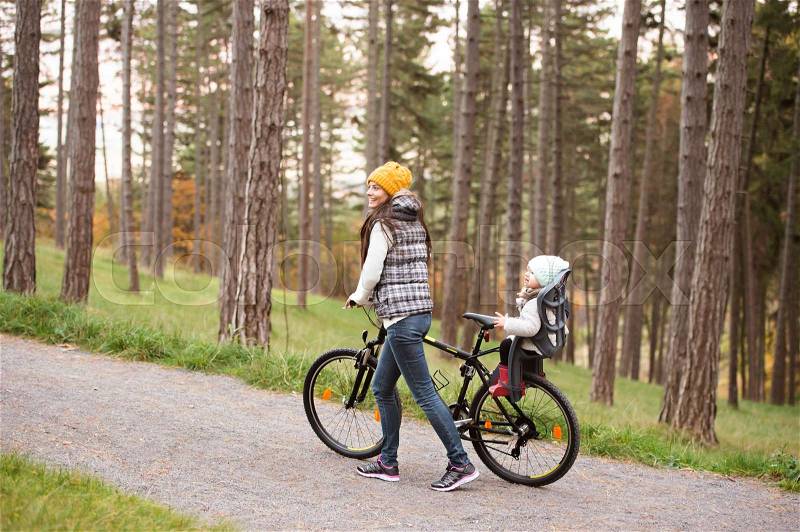 Beautiful young mother with her daughter in warm clothes on bicycle outside in autumn nature, stock photo