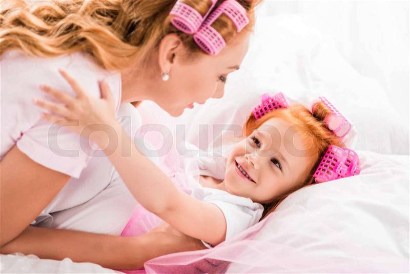 Side view of sensual mother and daughter hugging each other while lying in bed, stock photo