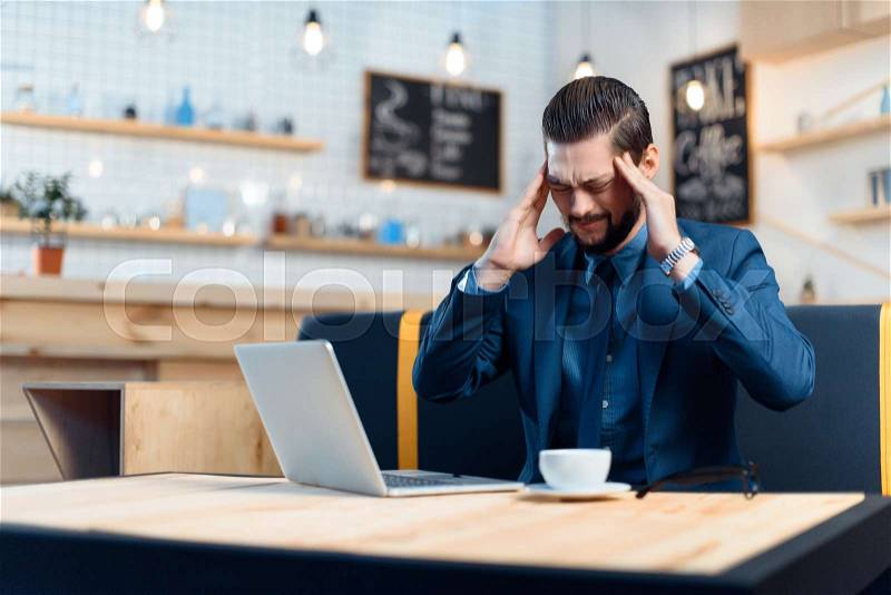 Overworked young businessman with headache using laptop in cafe, stock photo