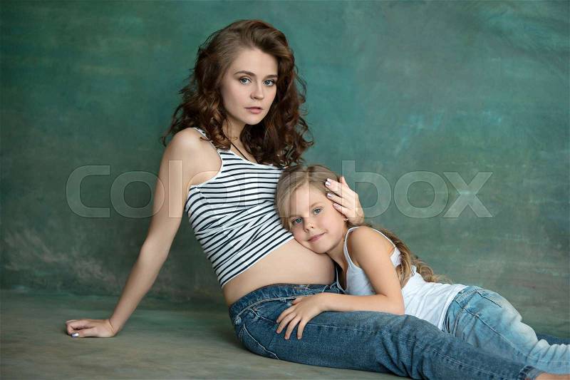 Pregnant mother with teen daughter. Family studio portrait over blue background. Teenager girl hugs her lovely mom, stock photo