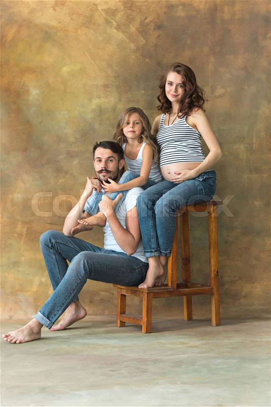 Pregnant mother with teen daughter and husband. Family studio portrait over brown background. Teenager girl hugs her lovely mom, stock photo