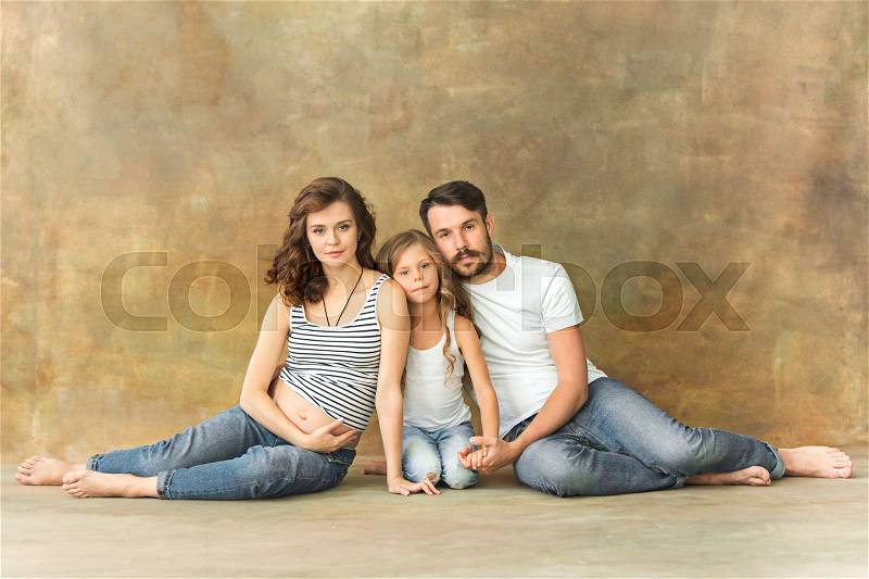 Pregnant mother with teen daughter and husband. Family studio portrait over brown background. Teenager girl hugs her lovely mom, stock photo