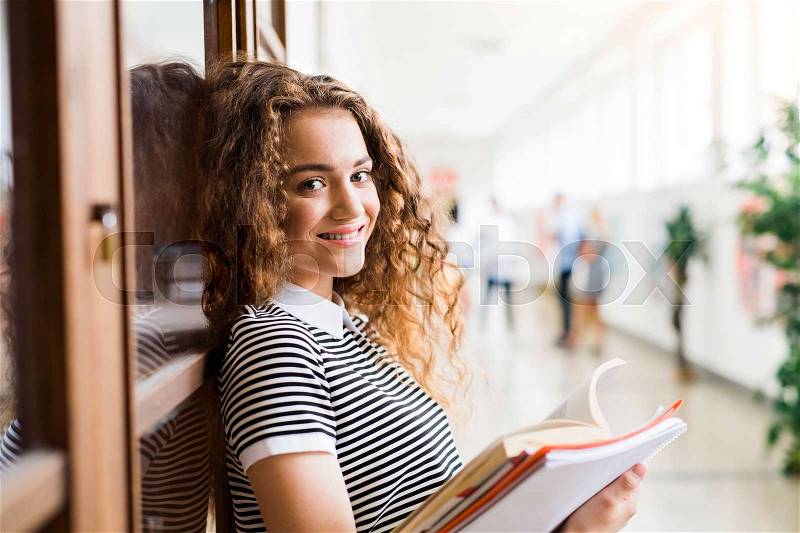 Attractive teenage girl with notebooks in high school hall during break, stock photo