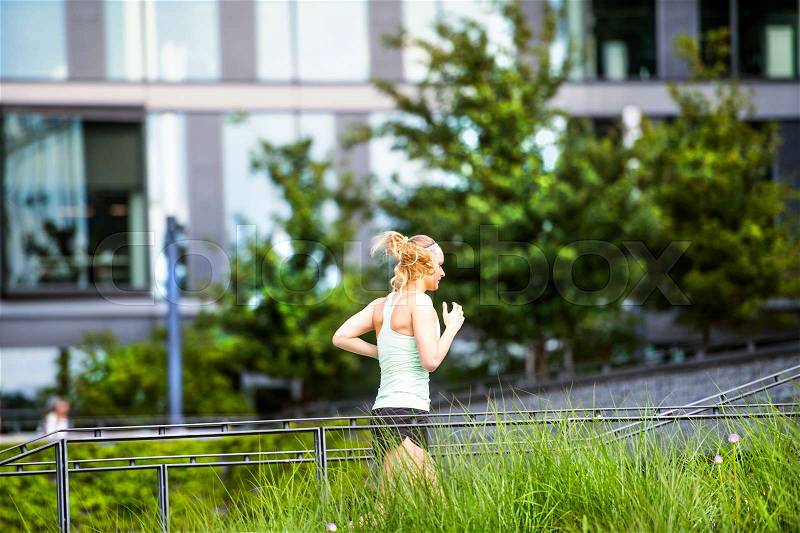 Beautiful young athlete in the city running in front of glass buildings, stock photo