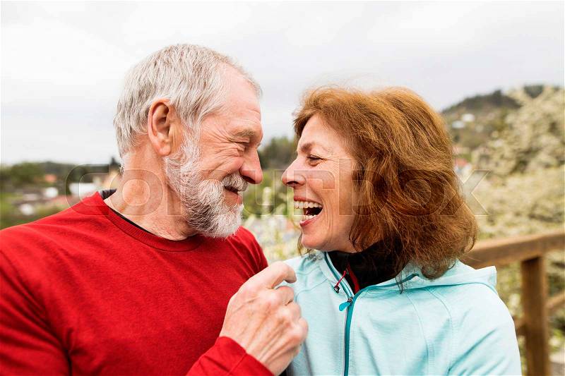 Beautiful active senior runners resting outside in sunny spring town, laughing, stock photo