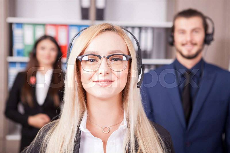 Portrait of beautiful blonde from customer support line next to two colleagues, stock photo