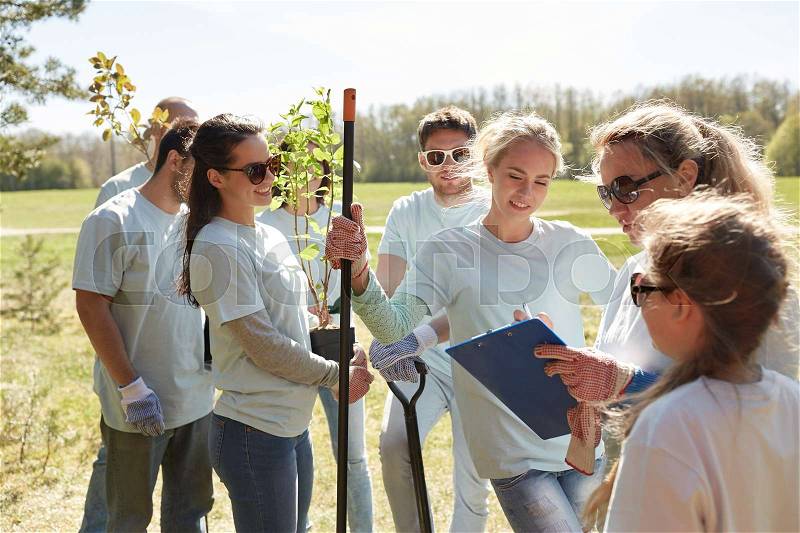 Volunteering, charity, people and ecology concept - group of happy volunteers with tree seedlings and clipboard in park, stock photo