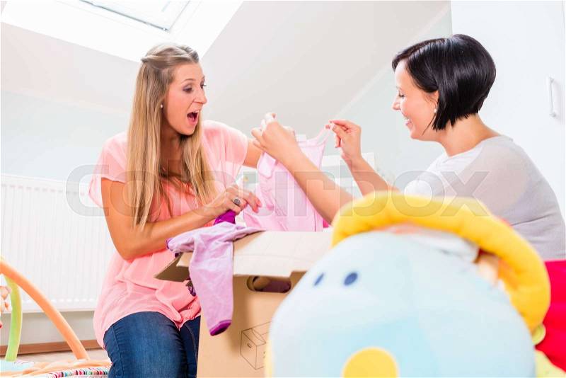 Pregnant woman and friend sharing baby clothes, stock photo