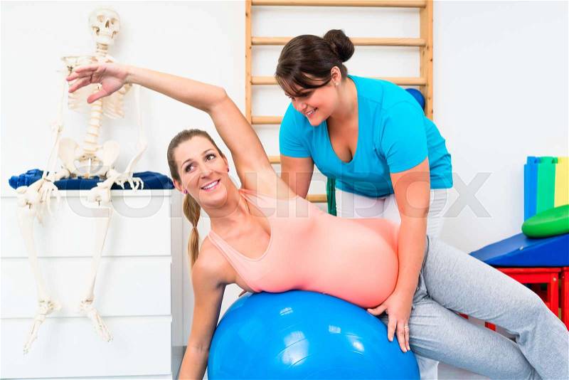 Pregnant woman exercising on swiss ball with physical therapist, stock photo