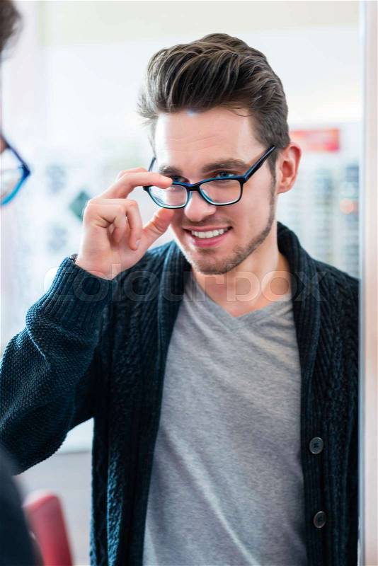Man testing glasses in optician shop mirror, stock photo
