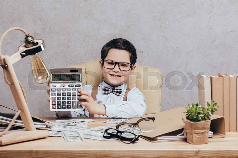 Portrait of smiling preteen boy in eyeglasses showing calculator in hands at workplace isolated on grey, stock photo