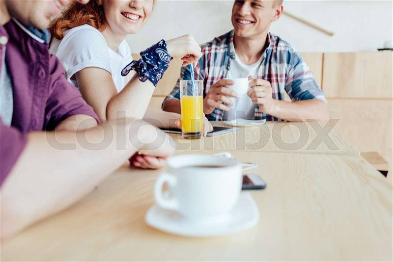 Smiling young friends drinking coffee and juice while talking in cafe, stock photo