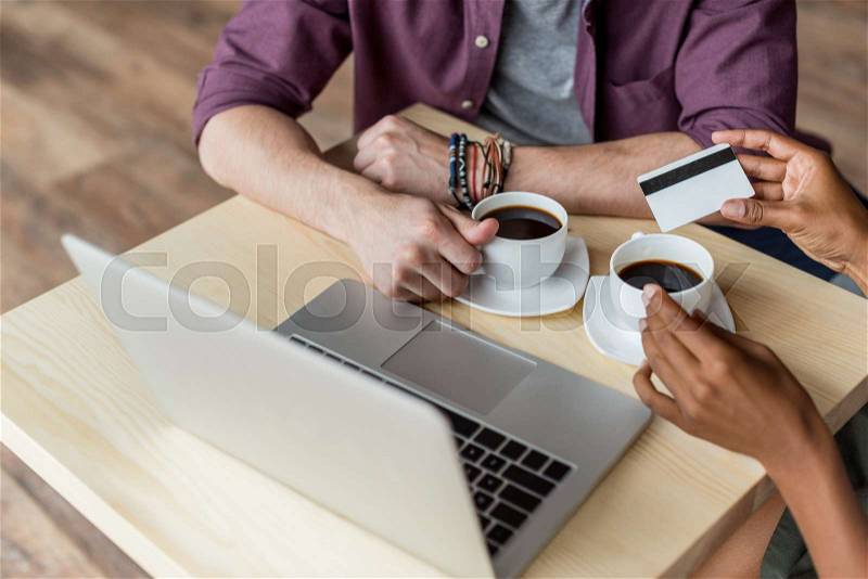 Cropped shot of young couple with credit card drinking coffee and using laptop at table, stock photo