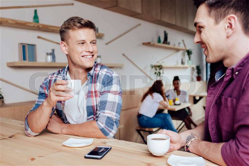 Handsome young men drinking coffee and talking in cafe, stock photo