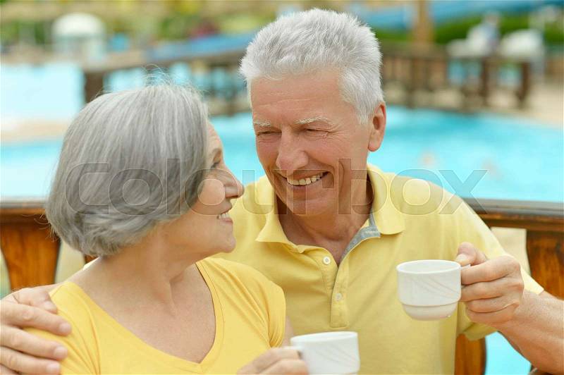 Smiling senior couple drinking coffee on blurred background, stock photo