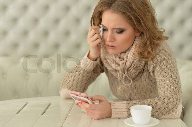 Portrait of a young beautiful crying woman using smartphone, stock photo