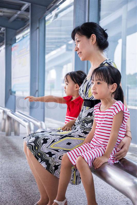 Asian Chinese mother and daughters waiting for a bus at bus stop, stock photo
