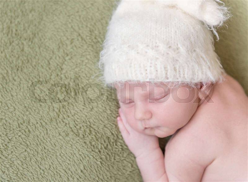 Lovely newborn baby in knitted hat sleeps curled up, top view, stock photo