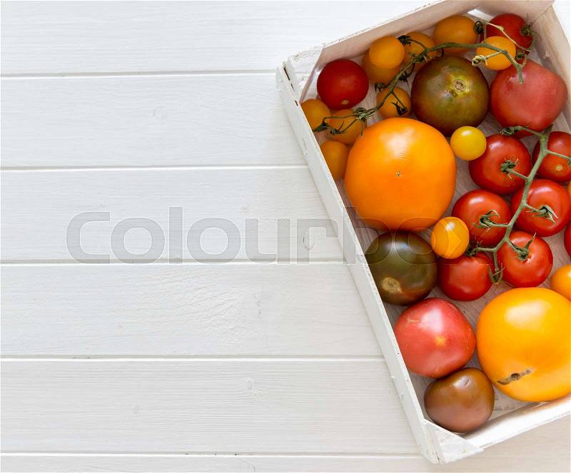 Variety of kinds of tomato in a box on a white wooden background, stock photo
