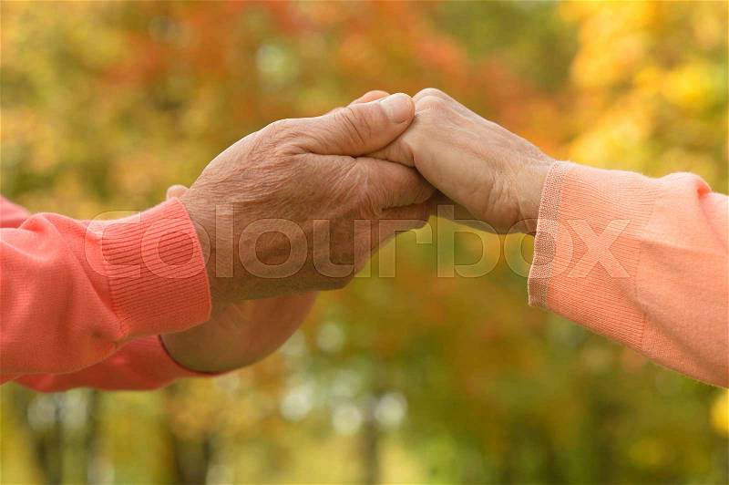 Elderly couple holding hands in autumn park, stock photo