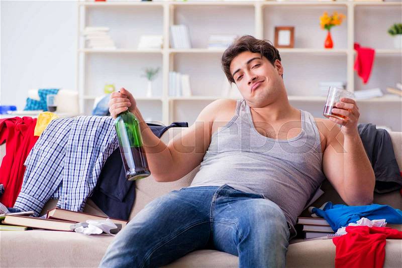 Young man student drunk drinking alcohol in a messy room, stock photo
