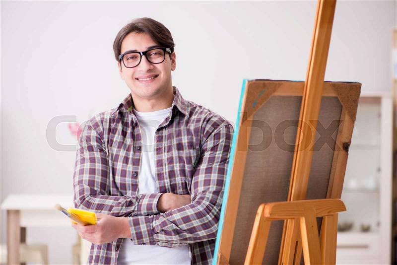 Young male artist drawing pictures in bright studio, stock photo