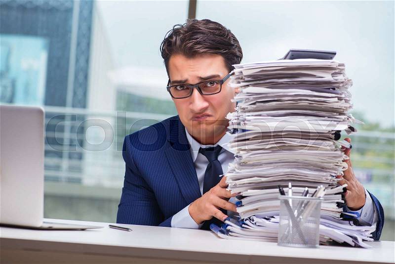 Businessman with pile stack of paper paperwork in the office, stock photo