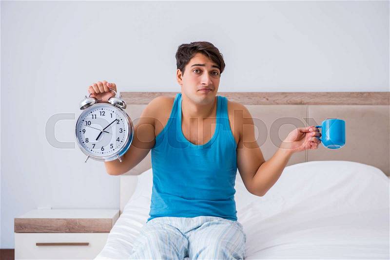 Young man waking up in bed, stock photo