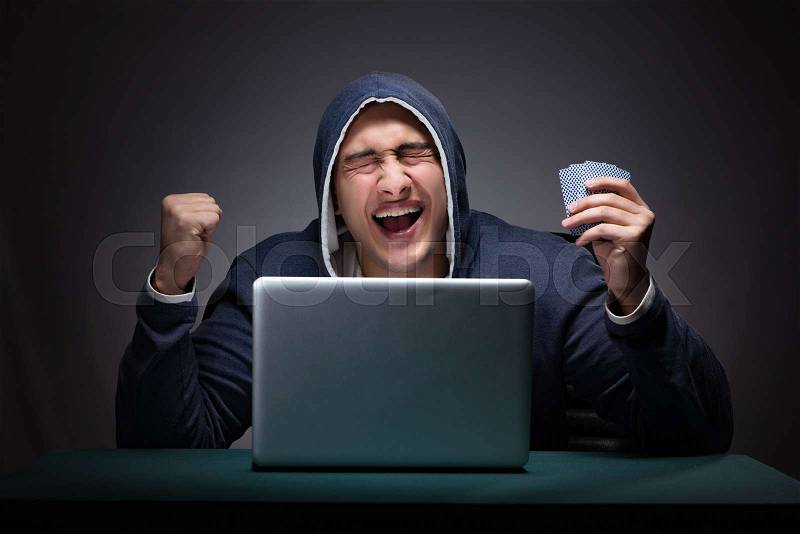 Young man wearing a hoodie sitting in front of a laptop computer gambling, stock photo