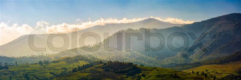 Panorama of mountainous rural area at sunrise. Gorgeous autumnal morning weather with clouds above the mountains and fog in valley, stock photo