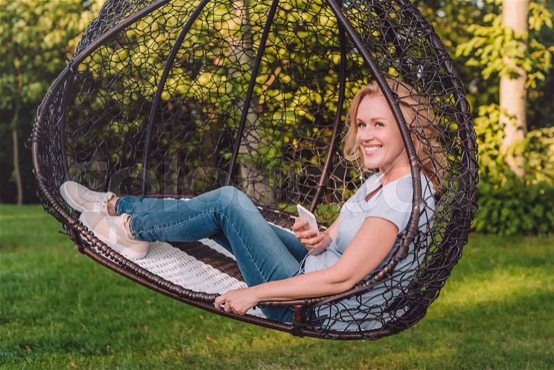 Smiling woman listening music in earphones while resting in garden , stock photo