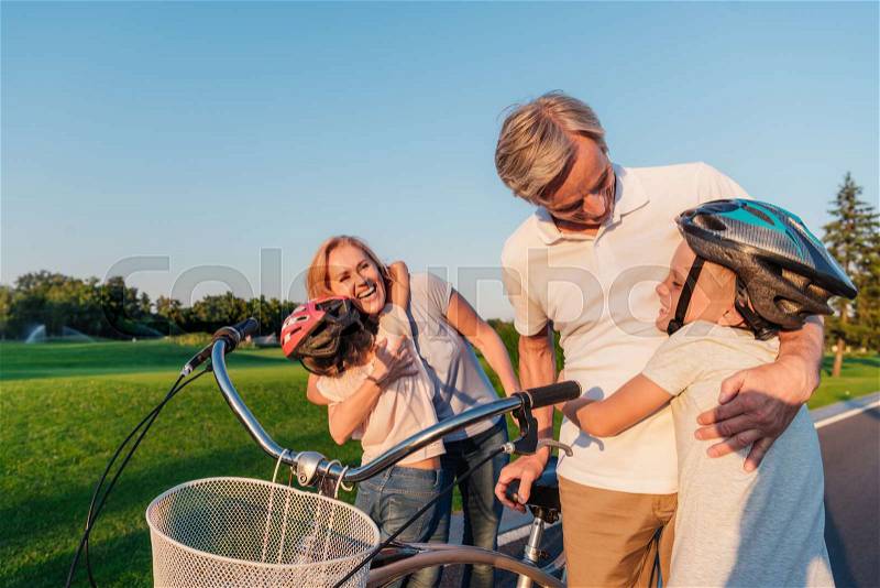 Children hugging happy grandparents while standing near bicycle, stock photo