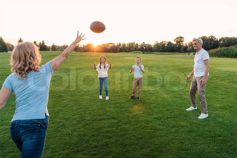 Happy grandparents playing american football with grandchildren in park, stock photo