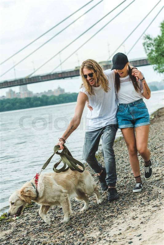 Happy beautiful young couple on walk with dog on beach, stock photo