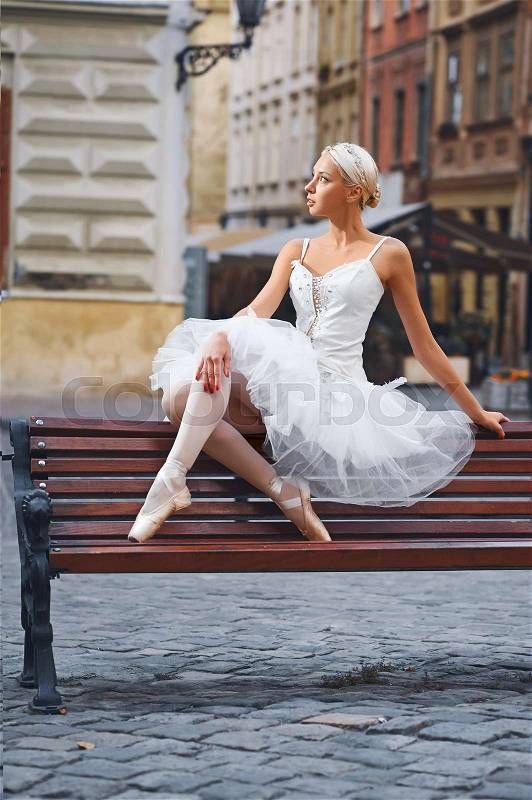 Full length shot of a beautiful ballerina sitting on the bench in the city center looking away thoughtfully, stock photo