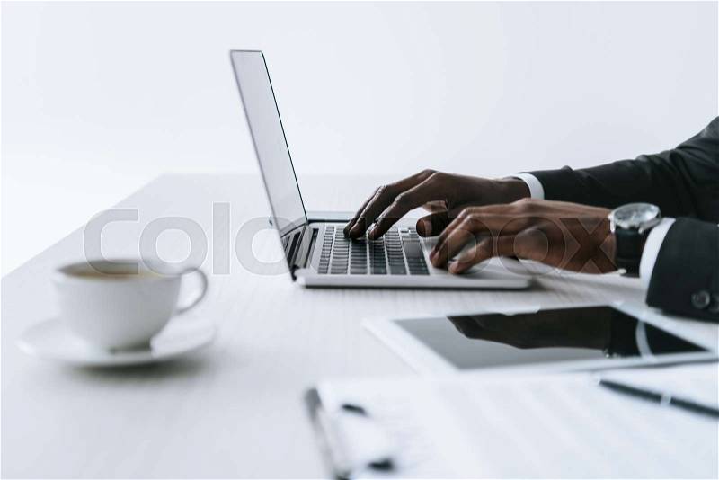 Partial view of african american businessman typing on laptop at workplace isolated on white, stock photo
