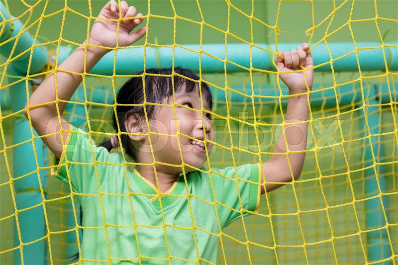 Asian Chinese little girl playing behind the net at indoor playground, stock photo