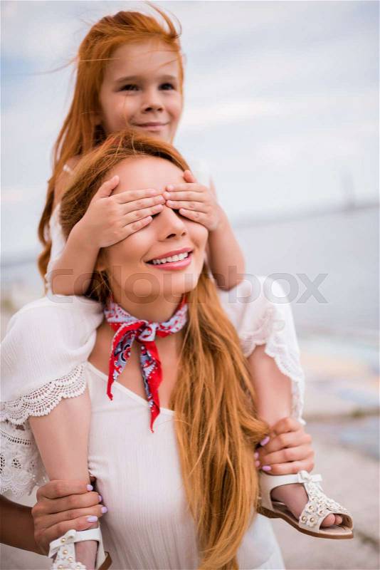 Happy young mother carrying adorable little daughter on neck, stock photo