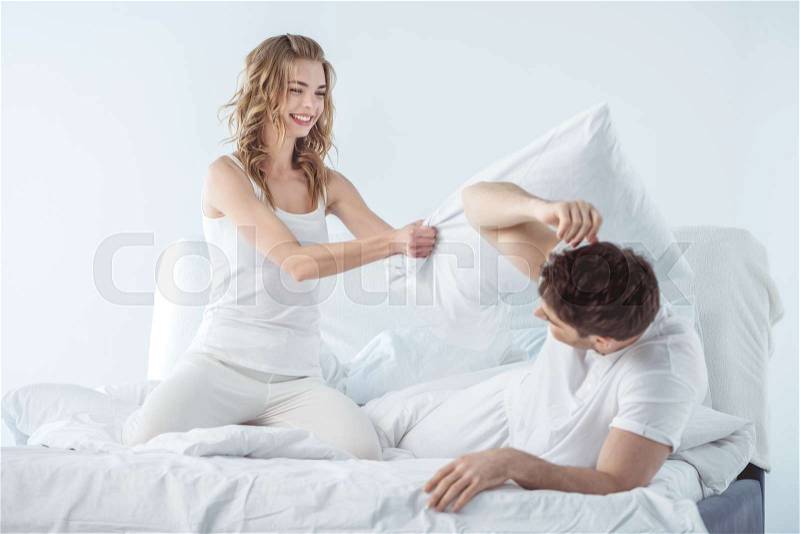 Young couple having pillow fight in bed , stock photo