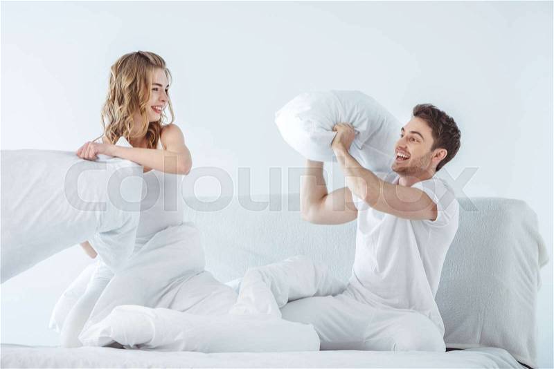 Young couple having pillow fight in bed, stock photo