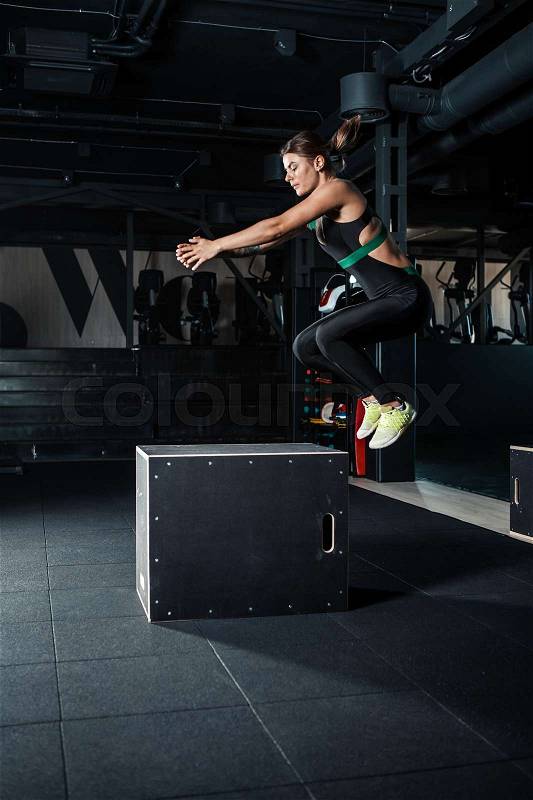 Young woman doing a box jump exercise. Muscular woman doing a box squat at the gym, stock photo